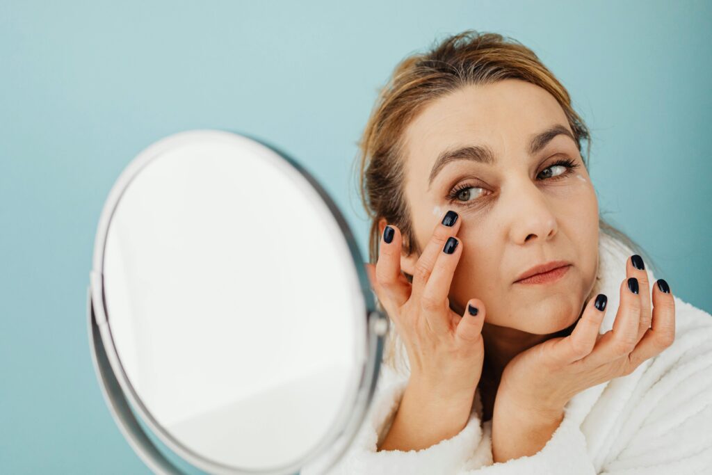 Woman applying sunscreen while looking in the mirror, practicing expert-recommended sun protection to manage rosacea flare-ups.