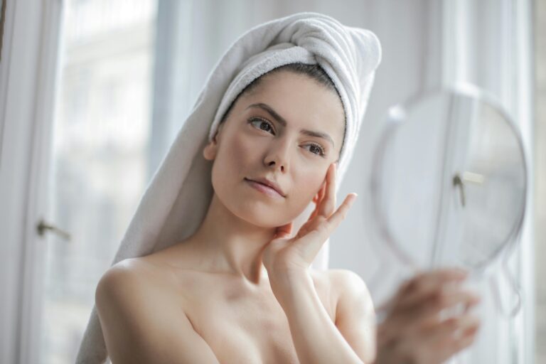 Woman examining her face in the mirror, thinking about the longevity of her dermal fillers.